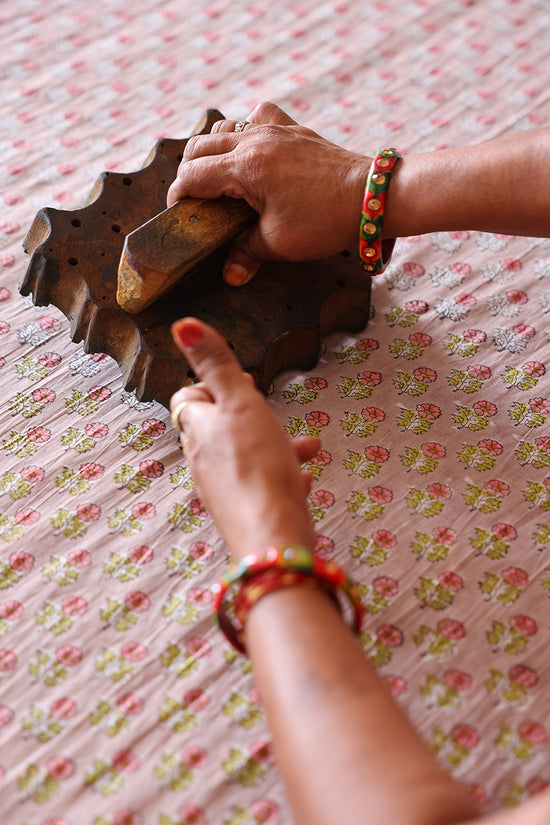 Indian artisan's hands placing a carved wooden block onto the Sunset floral print cotton fabric, demonstrating traditional hand block printing for Daughters of India garments