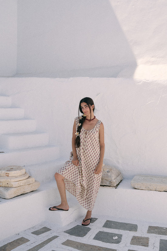 Woman in a whitewashed Greek architectural setting wearing the Daughters of India Sundress Midi in Peony, with flip flops and braided hair accessory